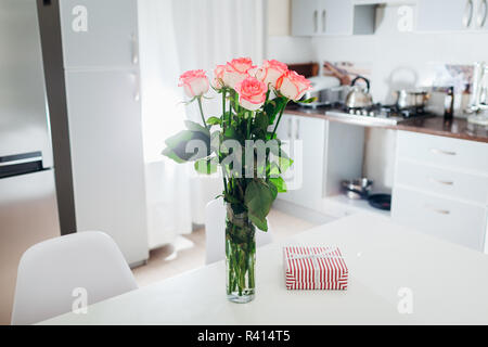 Blumenstrauß aus Rosen geschmückt mit Karte und Geschenkkarton links in die Küche. Überraschung für Frau. Valentinstag. Moderne Küche Design. Stockfoto