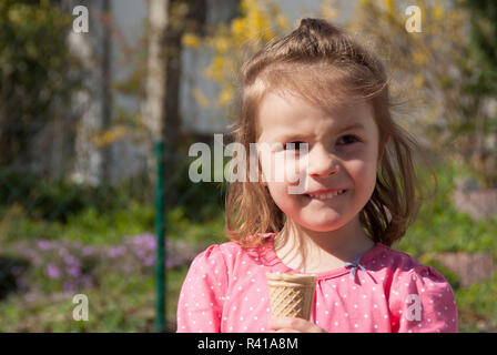 Ein kleines Mädchen steht mit einem Eis in den Garten und schaut sich fragend Stockfoto