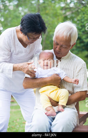 Asiatische schreiendes Baby getröstet von Großeltern im Garten Stockfoto