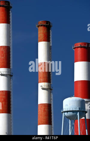 Ein Trio der roten und weißen Schornsteinen neben einem Wasserturm. Stockfoto