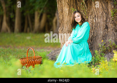 Eine Mädchen in einem langen Kleid setzte sich an einen Baum weiter, um den Warenkorb zu legen Stockfoto