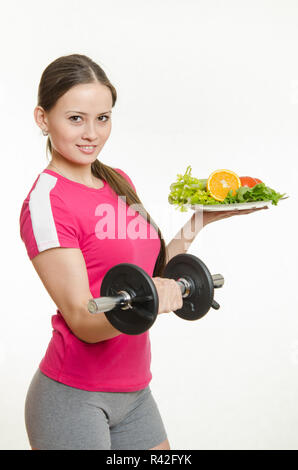 Halten Sie eine Kurzhantel und eine Obstschale Sportlerin Stockfoto