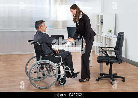 Geschäftsfrau Händeschütteln mit Geschäftsmann auf Rollstuhl Stockfoto