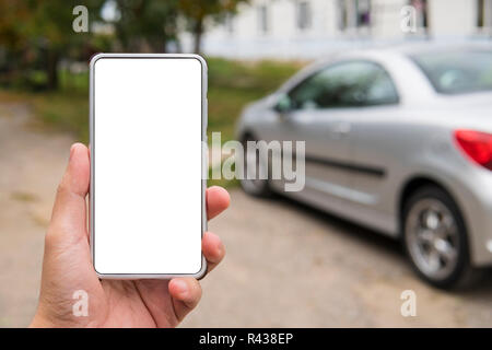 Mann hält eine Leere - Screen Smartphone in der linken Hand in der Nähe des abgestellten Fahrzeugs. Person auf der Straße mit dem Auto link Anwendung auf Handy. Remote engi Stockfoto