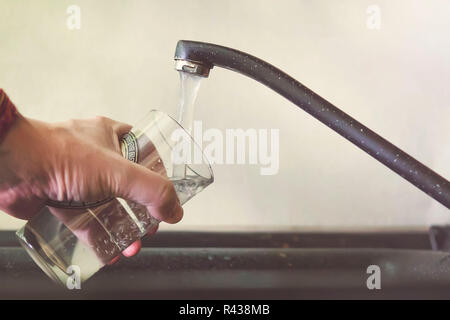 Füllung Glas mit Leitungswasser. Moderne Hahn und Waschbecken in der Küche zu Hause. Man gießt frisches zu trinken. Ein Mann gießt Wasser in ein Glas transparent g Tippen Stockfoto