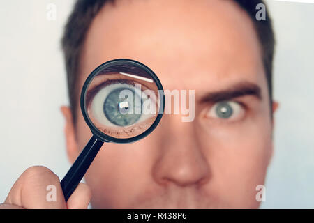 Nahaufnahme des Gesichts des Mannes mit der Lupe in der Nähe ein Auge auf weißem Hintergrund. Blick auf die Runde menschlichen Auge durch das magnifiying Glas. Neugierige Forscher. Durch die Lupe aufmerksam. Auge konzentrieren. Stockfoto