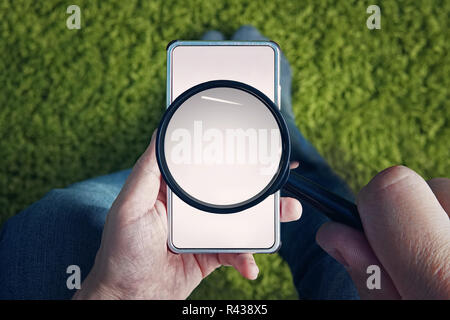 Ansicht von oben zu sitzen Menschen mit leeren Smartphone und Lupe über den Bildschirm. Mann hält Lupe etwas in das mobile Internet zu finden. Verwenden des Mobiltelefons zur Suche von Informationen online. Stockfoto