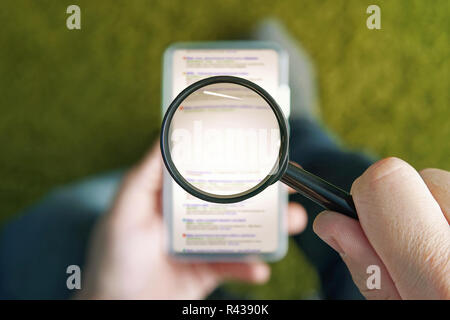 Mann sitzend mit transparenten Lupe über dem Smartphone surfen Suchmaschine Seite. Kopieren Sie Raum für Ihre Worte in der Mitte der Lupe über den mobilen Bildschirm. Konzept der Verwendung von Handy, Internet. Stockfoto