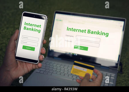 Man durchsucht Homepage von Internet banking Service auf seinem Smartphone und Laptop mit Kreditkarte. Online Payment mobile Banking Konzept. Geschrieben Worte Internet Banking auf dem Telefon und Notebook Bildschirme. Stockfoto