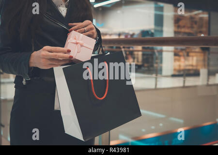 Geschenk Taschen in den Händen der Mädchen, auf dem Hintergrund, Shopping Mall. Shopping, Geschenke, Verkauf, shopping. Frau setzt eine Geschenkverpackung in einem schwarzen Gehäuse. Stockfoto