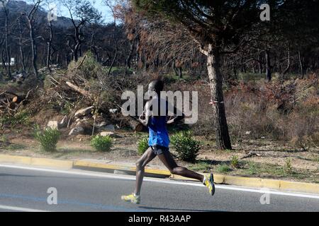 Die Teilnehmer laufen hinter einem verbrannten Fläche von Mati Dorf, wo 99 Menschen bei einem Waldbrand im letzten Sommer gestorben, während der Athen Marathon 2018. Stockfoto