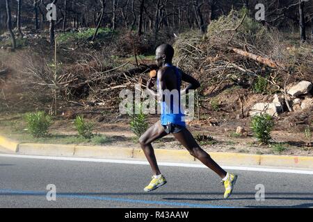 Die Teilnehmer laufen hinter einem verbrannten Fläche von Mati Dorf, wo 99 Menschen bei einem Waldbrand im letzten Sommer gestorben, während der Athen Marathon 2018. Stockfoto