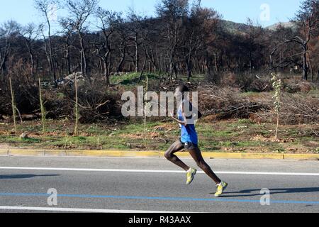 Die Teilnehmer laufen hinter einem verbrannten Fläche von Mati Dorf, wo 99 Menschen bei einem Waldbrand im letzten Sommer gestorben, während der Athen Marathon 2018. Stockfoto