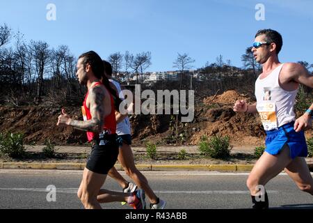 Die Teilnehmer laufen hinter einem verbrannten Fläche von Mati Dorf, wo 99 Menschen bei einem Waldbrand im letzten Sommer gestorben, während der Athen Marathon 2018. Stockfoto