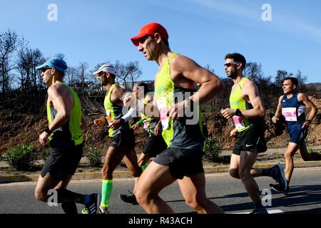 Die Teilnehmer laufen hinter einem verbrannten Fläche von Mati Dorf, wo 99 Menschen bei einem Waldbrand im letzten Sommer gestorben, während der Athen Marathon 2018. Stockfoto