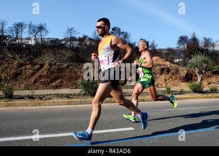 Die Teilnehmer laufen hinter einem verbrannten Fläche von Mati Dorf, wo 99 Menschen bei einem Waldbrand im letzten Sommer gestorben, während der Athen Marathon 2018. Stockfoto