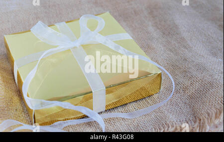 Gold Geschenkbox mit weißem Band auf der braunen Sack. Stockfoto