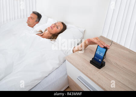 Frau im Bett dösen Wecker am Handy Stockfoto