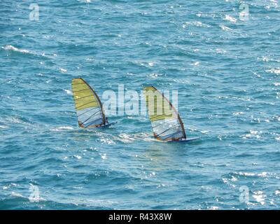 Zwei Windsurfer gehen unter der grellen Sonne in schwerer See im Meer bei hohen Geschwindigkeiten Stockfoto