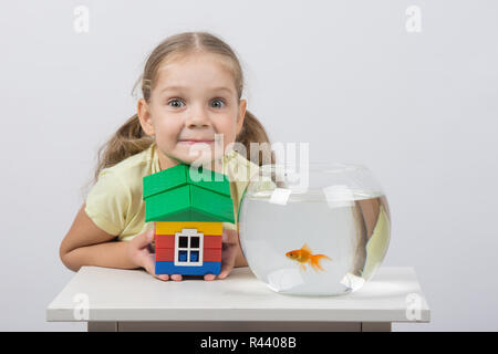 Vierjährige Mädchen hält ein Spielzeug Haus und sitzt vor der einen Goldfisch Stockfoto