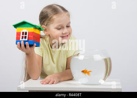 Das vierjährige Mädchen sitzt mit einem Spielzeug-Haus vor einem Goldfisch Stockfoto