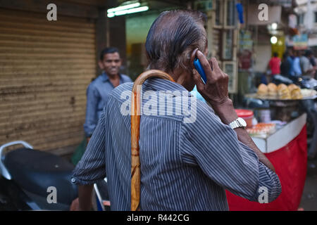 Hände frei: Ein mobiler Benutzer in einem Markt, in Mumbai, Indien, finden eine intelligente Weise seinen Spazierstock zu tragen, wenn sie nicht in Gebrauch Stockfoto