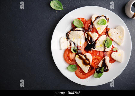 Valentinstag Salat. Klassische italienische Caprese Salat mit Herz gebildet, Mozzarella, Basilikum, Balsamico und Tomaten auf dem Teller serviert. Oben betrachten. Kopieren spa Stockfoto