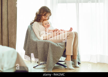 Eine Mutter mit einem Baby auf dem Arm sitzt auf einem Stuhl. Stockfoto