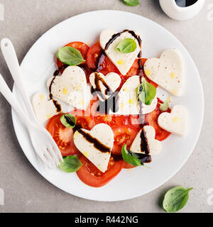 Valentinstag Salat. Klassische italienische Caprese Salat mit Herz gebildet, Mozzarella, Basilikum, Balsamico und Tomaten auf dem Teller serviert. Oben betrachten. Platz. Stockfoto