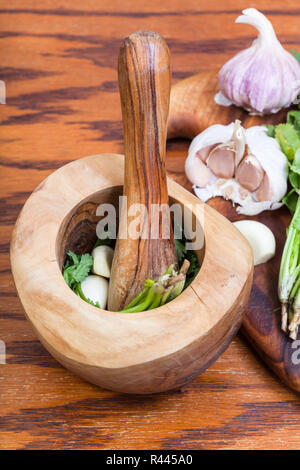 Holz Mörser mit Koriander Kraut und Knoblauch auf Tisch Stockfoto