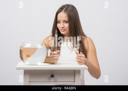 Mädchen mit Messer und Gabel in der Hand und mit Appetit für den Blick auf die kleine Goldfische Stockfoto