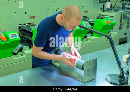 Arbeiter in der Print Factory, neben dem Flexo Maschine vorbereiten Photopolymer relief Platte auf einem Druckzylinder stehen. Szene mit Halterung Stockfoto