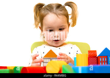 Toddler girl spielt mit bunten Holzklötzen auf weißen Hintergrund. Kleinkind baut ein Haus aus Bausteinen. Blondes Haar kleinkind Mädchen spielt wi Stockfoto