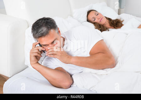 Mann Besetzt bei Telefon, während Frau schlafen Stockfoto