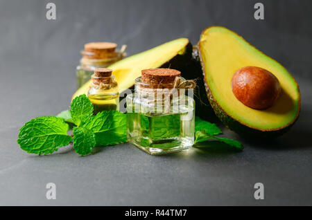 Avocadoöl und Geschnittene frische Avocado auf schwarzem Stein. Organische Kosmetik öl Konzept Stockfoto