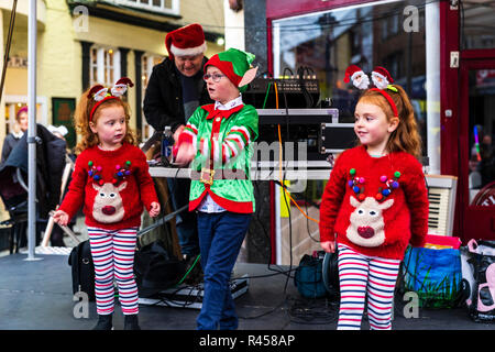 Drei jungen kaukasischen Kinder, ein Junge, zwei Mädchen, 6-7 Jahre alt, gekleidet wie Santa's Elfen auf der Open Air Bühne tanzen während der Weihnachtsfeier. Stockfoto