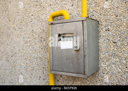 In der Nähe von Metall Stahl Gaszähler Box mit Anschluss gelben Leitungen hängen auf Exterieur Licht Haus aus Stein Wand. Bau, Renovierung, Messung t Stockfoto