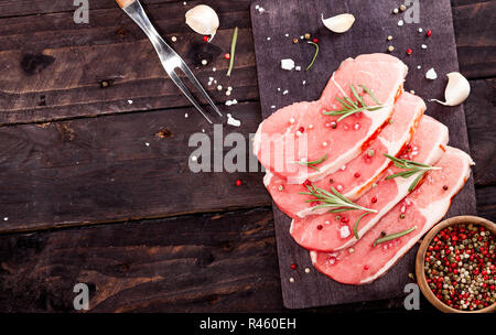 Rohes Fleisch. Rohes Rindfleisch Steak auf einem Schneidebrett mit Rosmarin und Gewürze auf einem schwarzen Hintergrund mit kopieren. Stockfoto