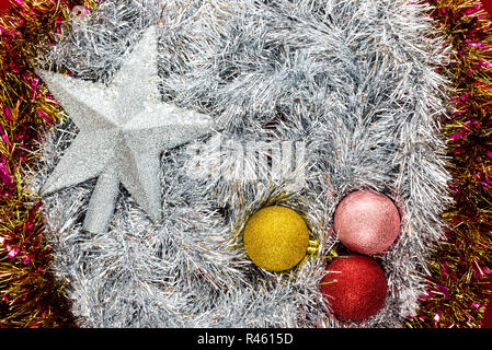 Drei Weihnachtskugeln und silbernen Sternen liegt auf einer Silber- und coloful Lametta Hintergrund, Weihnachtsschmuck. Stockfoto