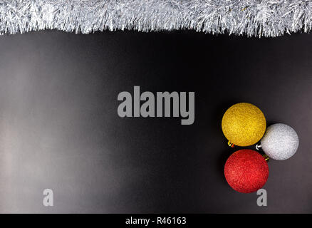 Drei Weihnachtskugeln liegt auf einem schwarzen Hintergrund mit wenig Licht mit silbernem Lametta, Weihnachtsschmuck. Stockfoto