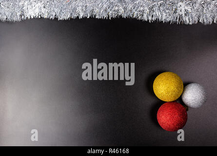 Drei Weihnachtskugeln liegt auf einem schwarzen Hintergrund mit wenig Licht mit silbernem Lametta, Weihnachtsschmuck. Stockfoto