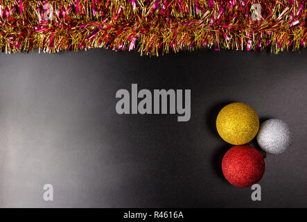 Drei Weihnachtskugeln liegt auf einem schwarzen Hintergrund mit wenig Licht mit bunten Lametta, Weihnachtsschmuck. Stockfoto