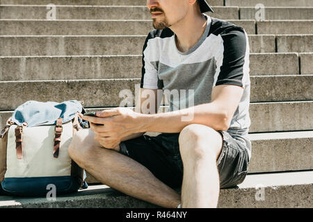Als Tourist oder Student sitzt auf der Treppe, ruht und verwendet ein Mobiltelefon. Stockfoto