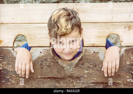 Jungen kaukasischen Jungen in mittelalterlichen Pranger. Elend Thema. Strafe Gerät. Gelb Foto Filter. Stockfoto