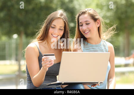 Zwei glückliche Freunde online bezahlen mit Kreditkarte und einen Laptop in einem Park Stockfoto