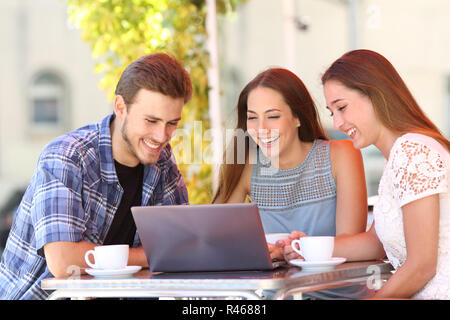 Drei glückliche Freunde gerade online die Inhalte auf den Laptop in einer Bar Stockfoto