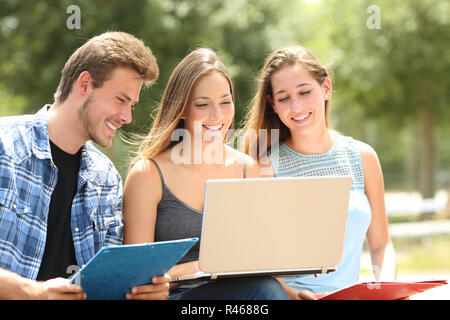 Drei glückliche Schüler e-Lernens zusammen sitzen auf einer Bank in einem Campus Stockfoto