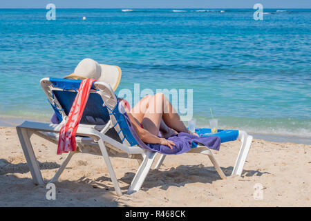 Latina Frau trägt einen Strohhut sitzend in einem Liegestuhl am Strand Playa Jibacoa auf der atlantischen Küste von Kuba. Stockfoto