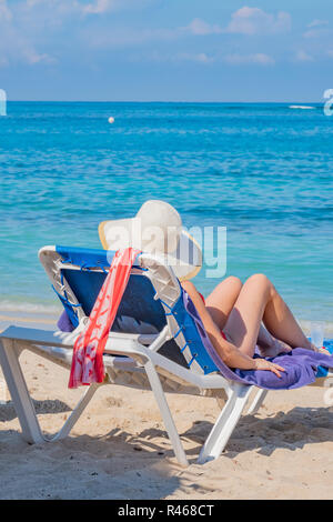 Latina Frau trägt einen Strohhut sitzend in einem Liegestuhl am Strand Playa Jibacoa auf der atlantischen Küste von Kuba. Stockfoto