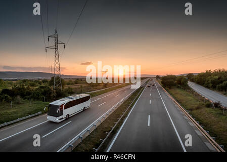 Bus Reisen auf eine einsame Landschaft Autobahn mit schönen Sonnenuntergang hinter Stockfoto